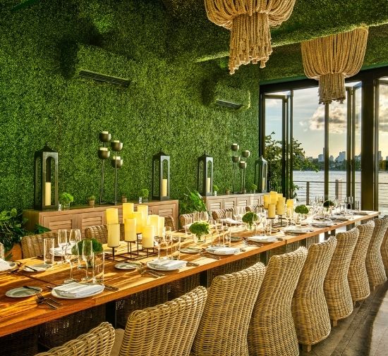 Large rectangular table set with glassware and table placements with a greenery wall behind it and a boho designed beaded chandelier