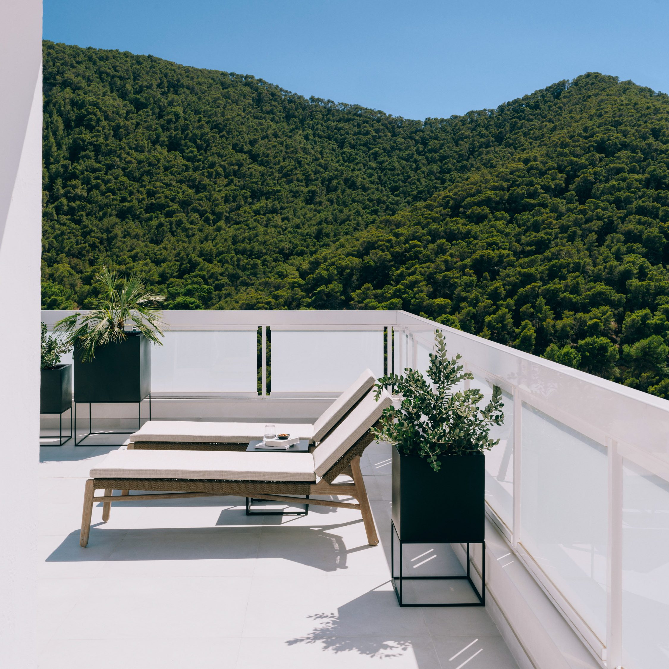 White terrace with two cushioned lounge chairs and green mountains in the background