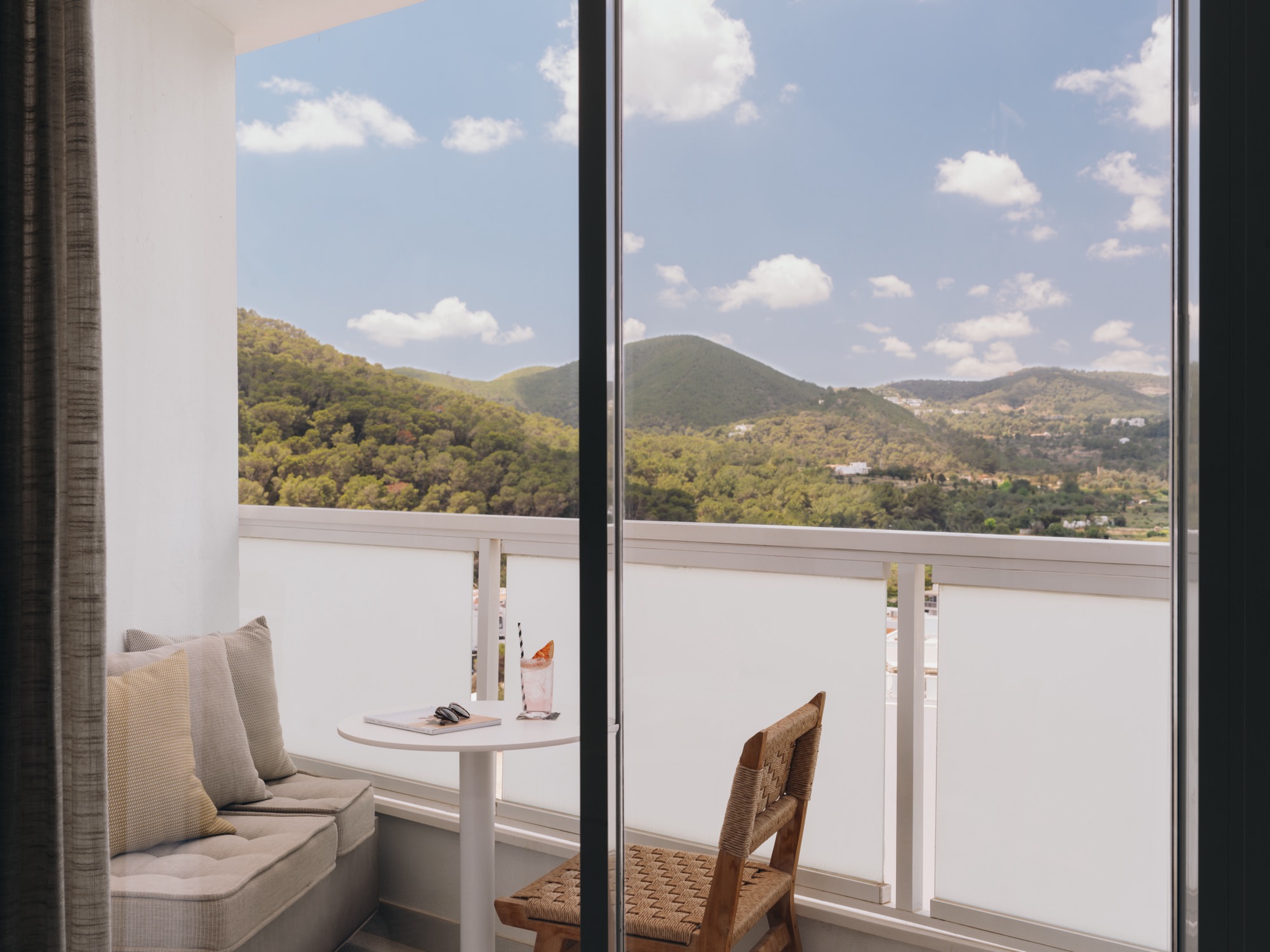 Suite tipo estudio en Mondrian ibiza . Balcón con cojines blancos, una silla y vistas a las montañas de Cala Llonga.