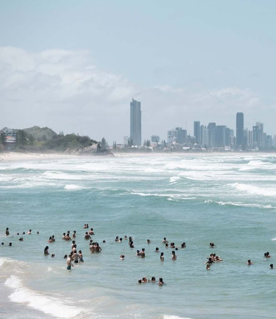 Beach with groups of people wading in the ocean and skyscrapers in the background