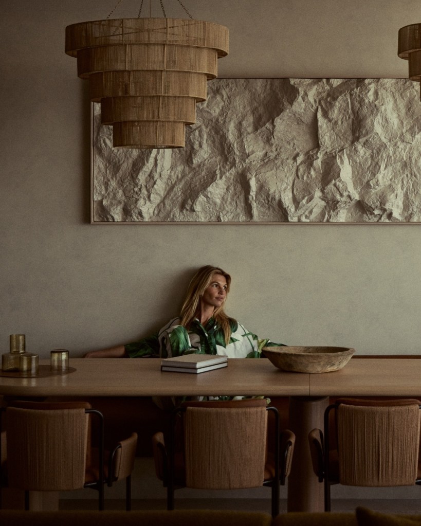 Woman sits at modern dining table with fringe chandelier above and textured artwork on the wall