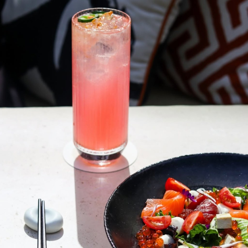 Pink cocktail and salad in the corner on a white table