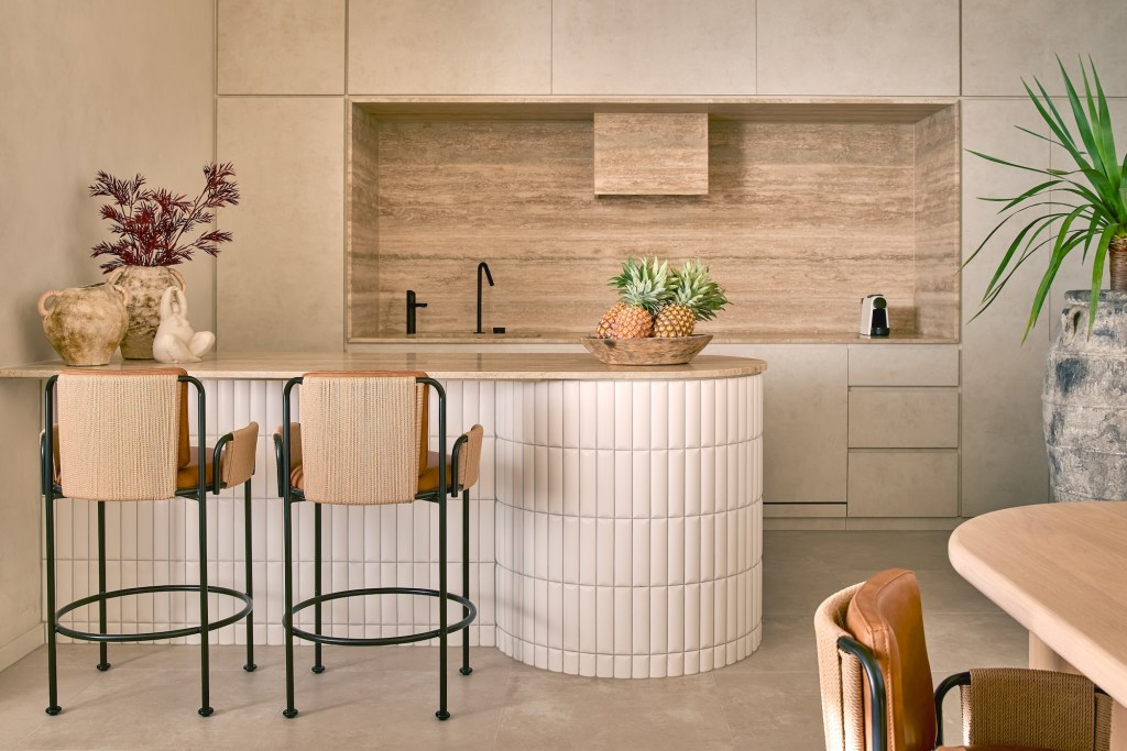 Kitchen with white island, two bar stools, and light wood finishes