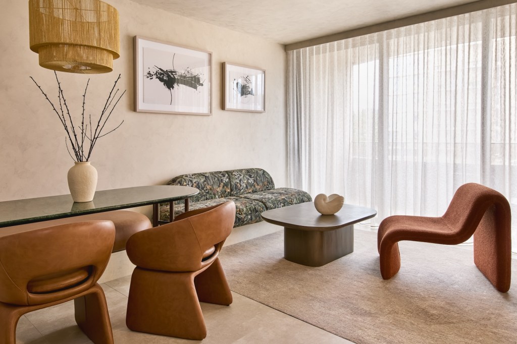 Angled view of an oval dining table with twigs on top and a patterned sofa, coffee table, and chestnut leather chair in the corner