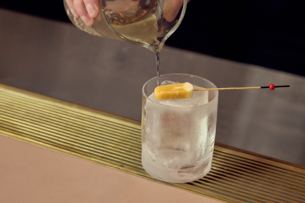 Clear cocktail being poured into a short frosted glass