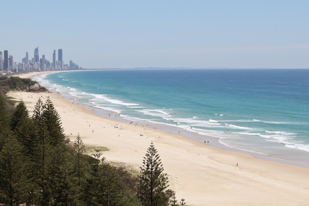 Sandy beach with bright blue water and cityscape in the distance