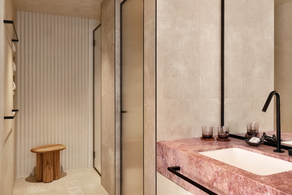 Pink marble bathroom sink with mirror above and walk-in shower in the distance