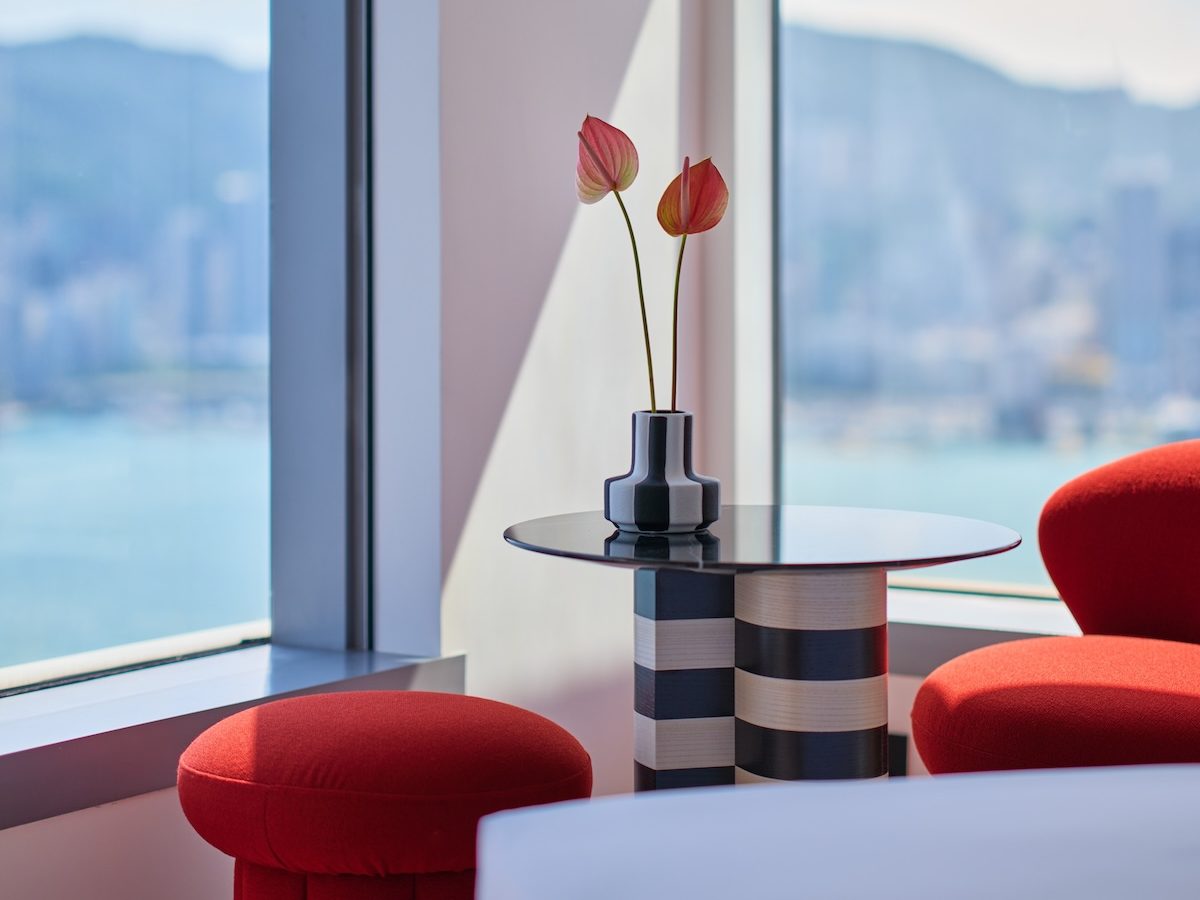 Black and white striped side table with small plant on it with windows with a city view in the background