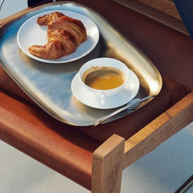 Croissant and coffee on a tray on a wooden chair with leather jacket slung over it and boots on the floor