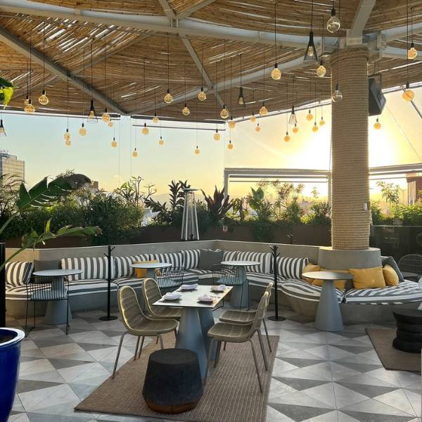 Rooftop bar with string lights, tables, and striped couches