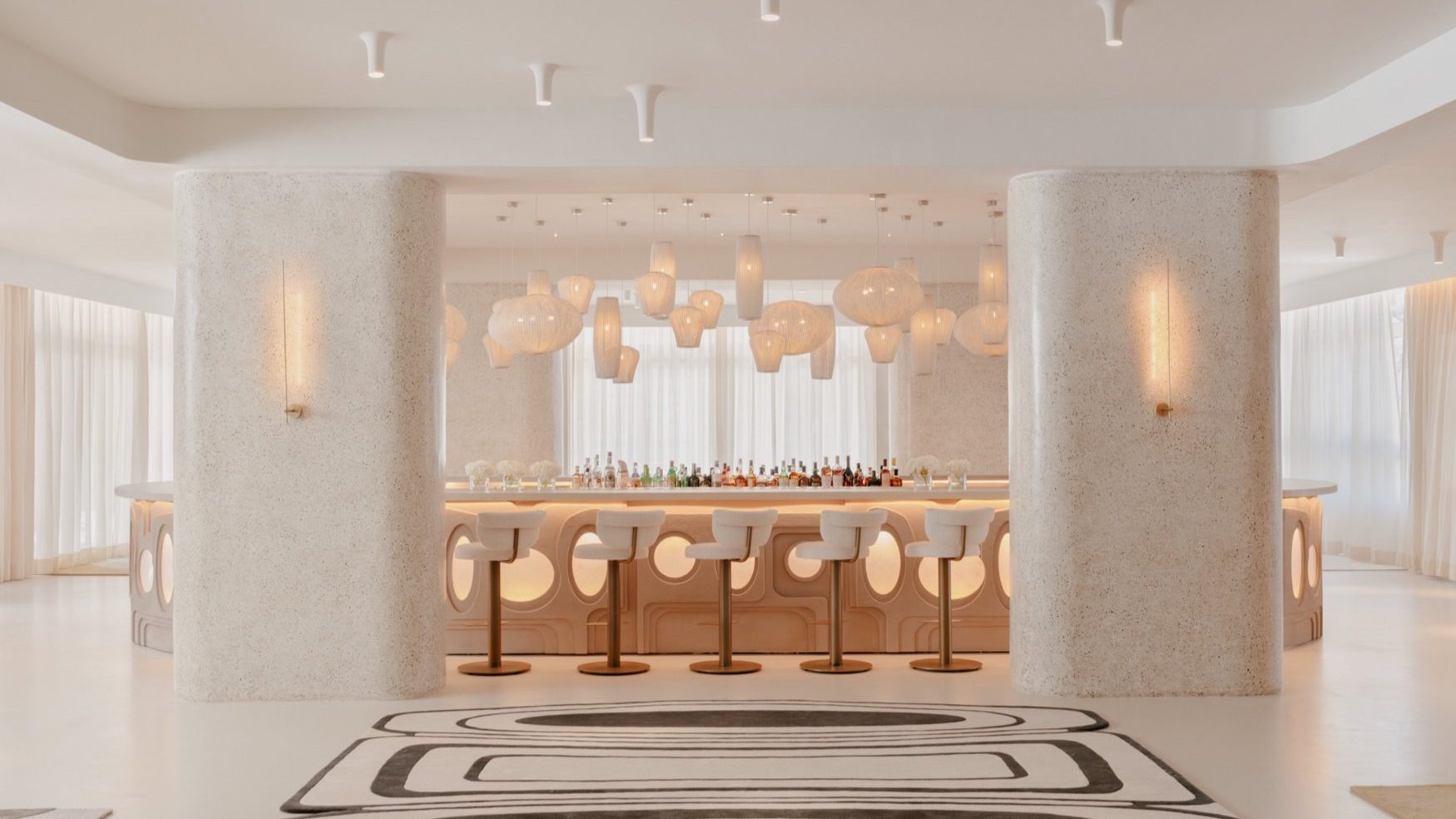 Beautiful modern white bar with white pendant lights, black and white geometric rug, and barstools.