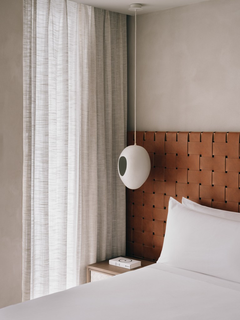 Good - Mondrian Ibiza Mondrian Sute, brown leather bed headboard, king size bed with white sheets, modern white hanging lamp, wooden bedside table and door towards a balcony facing mountain views