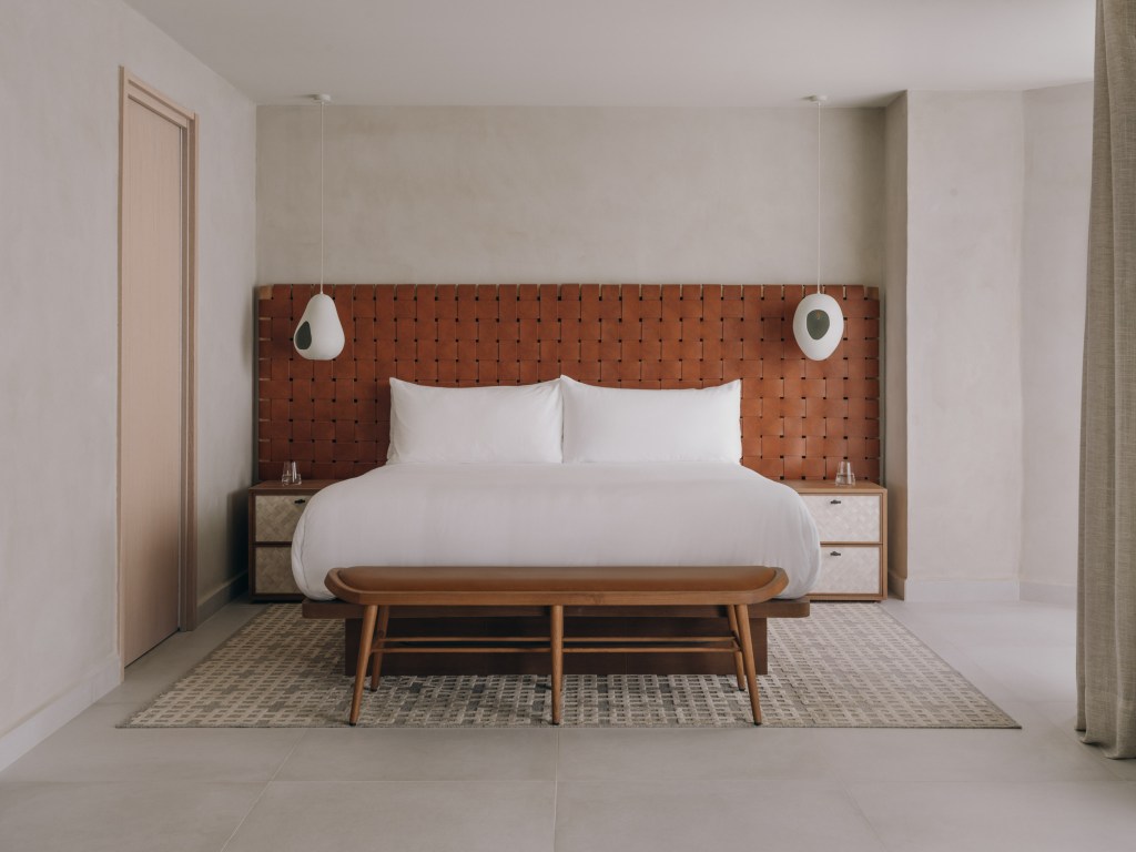 Mondrian Ibiza Panoramic Suite king size mattress which white sheets brown leather headboard with two bedside tables, a carpet and two modern lamps