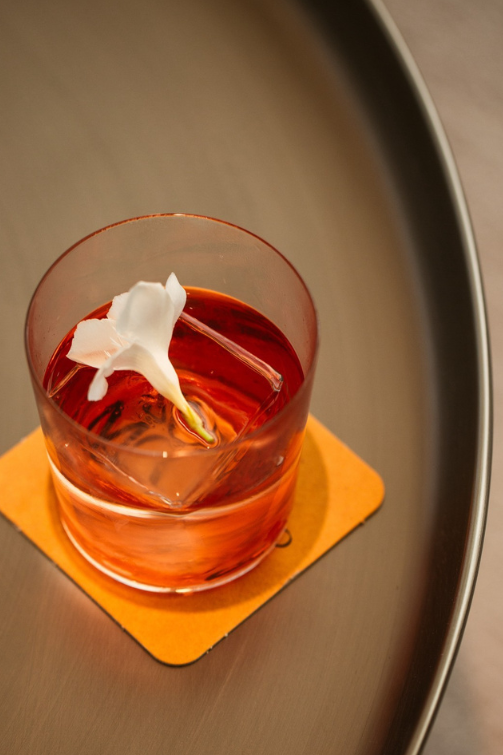 a pink cocktail in a small glass garnished with a white flower