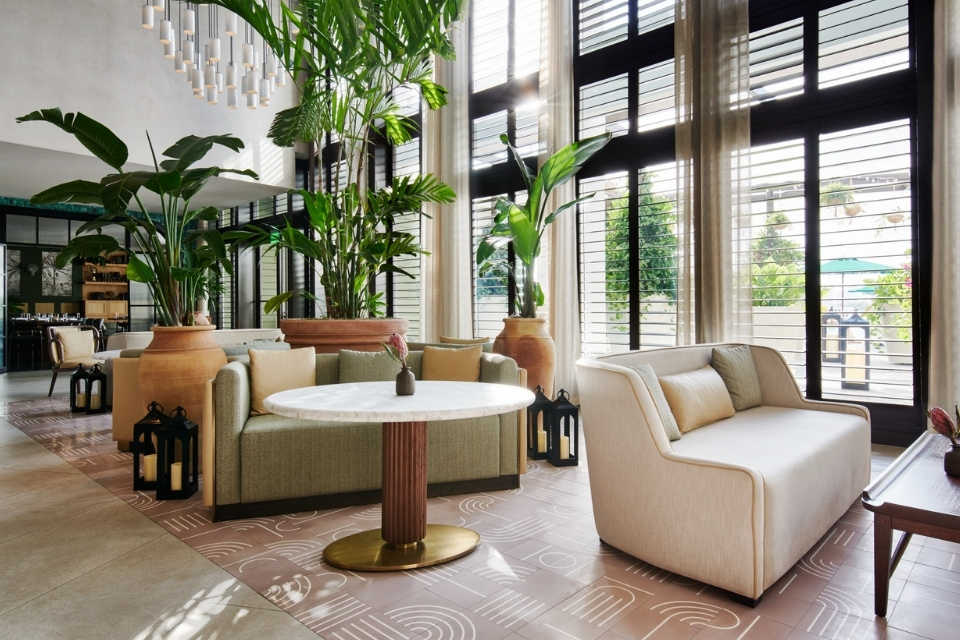 Naturally lit hotel lobby with neutral colored sofas and palm trees