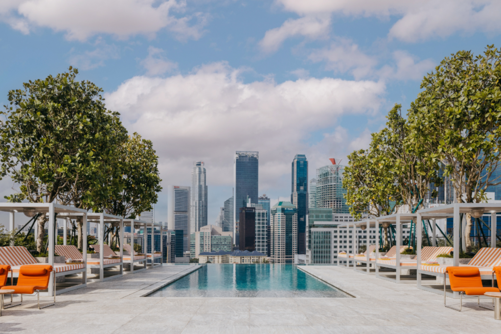 Rooftop pool lined with striped cabanas on both sides and cityscape in the background