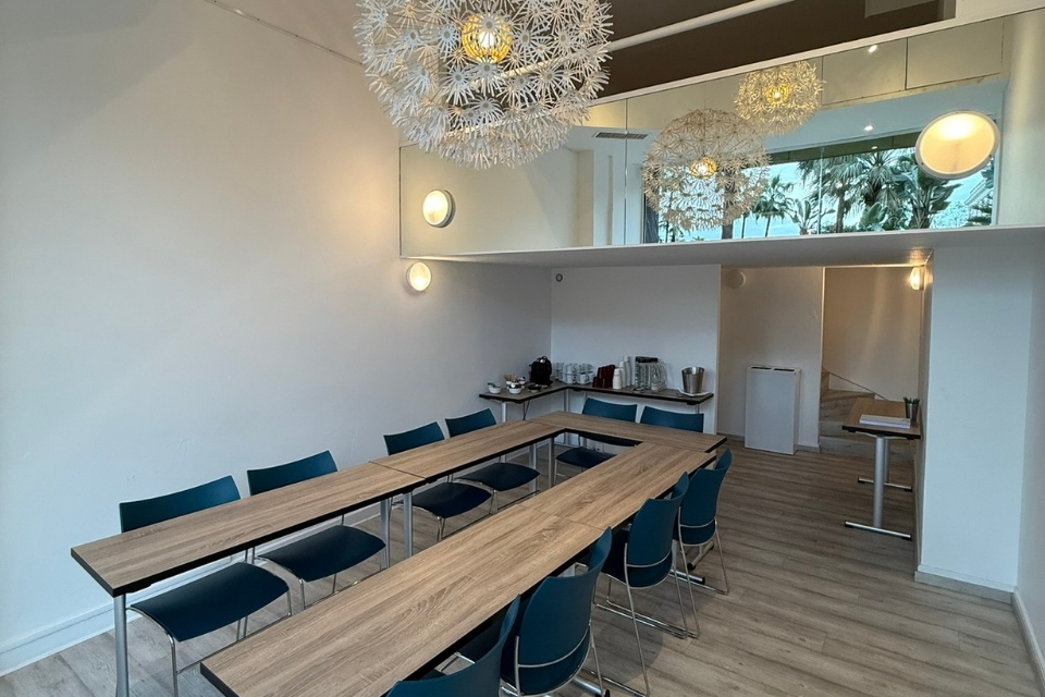 Large wooden desks in a U-Shape in a meeting room with white flowery chandeliers