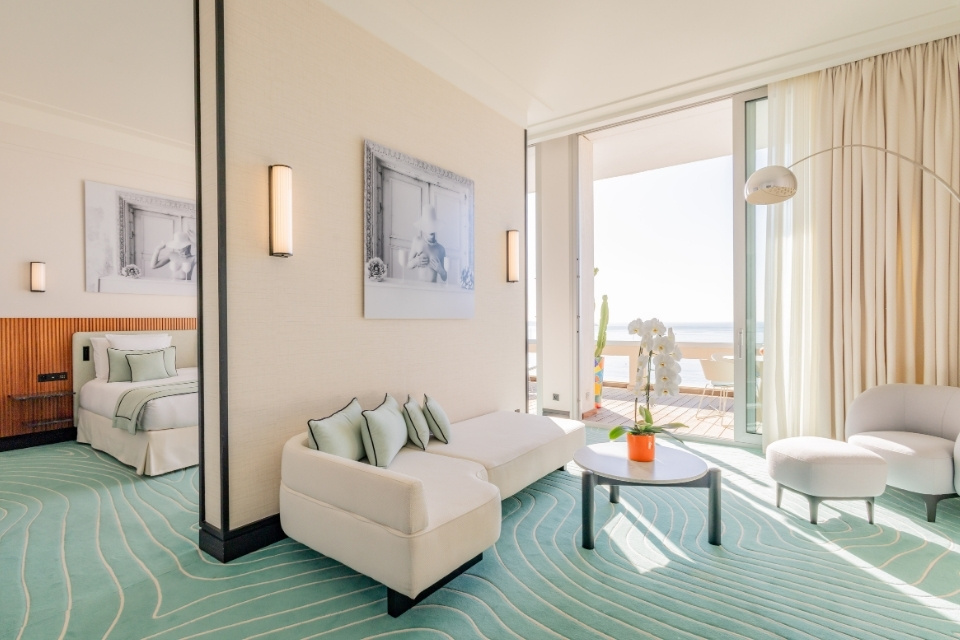 Hotel suite with turquoise carpet, cream sofa, and large bed in the background