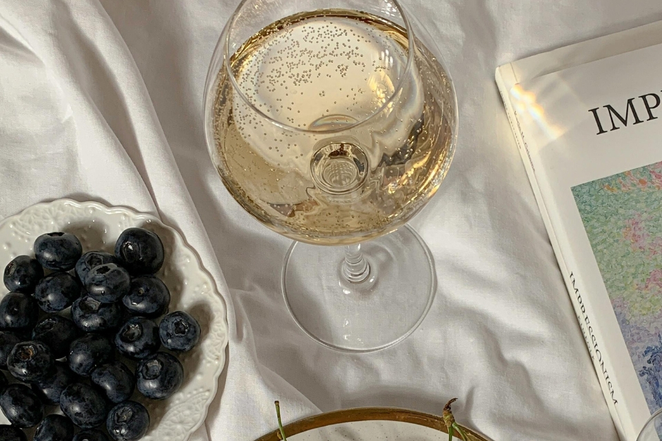 Glass of champagne and plate of blueberries on white sheets