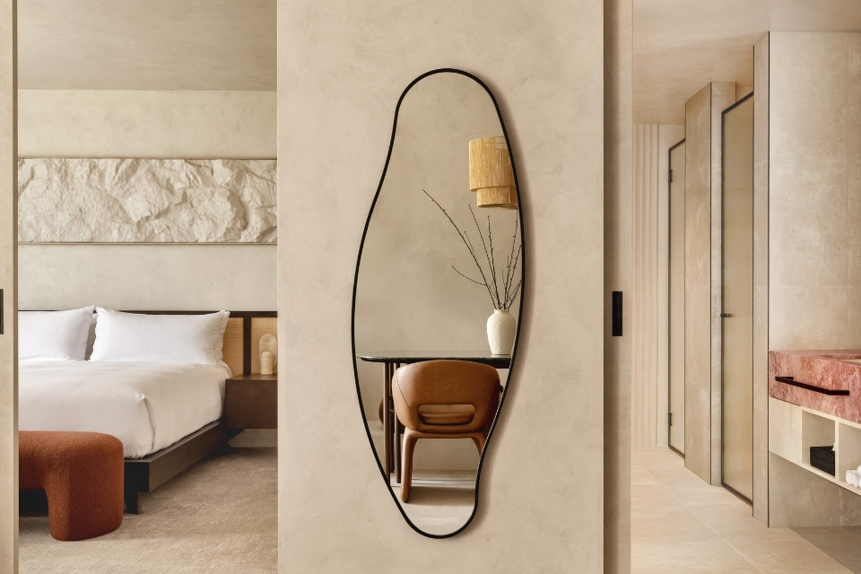 Large hotel suite with large white bed, curved mirror on wall, and bathroom with pink marble sink