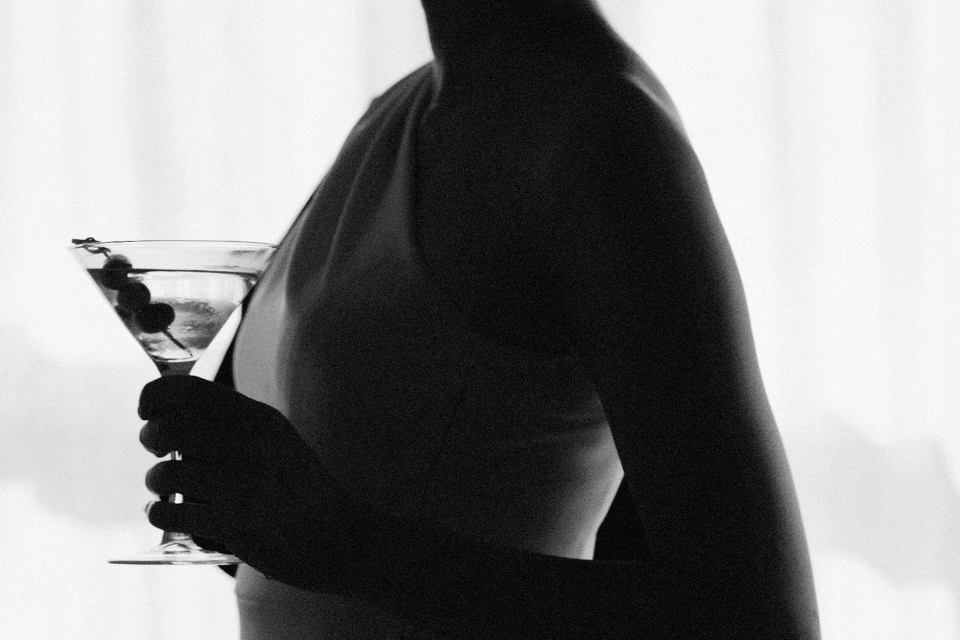 Dark image of a woman holding a martini glass with olives in it
