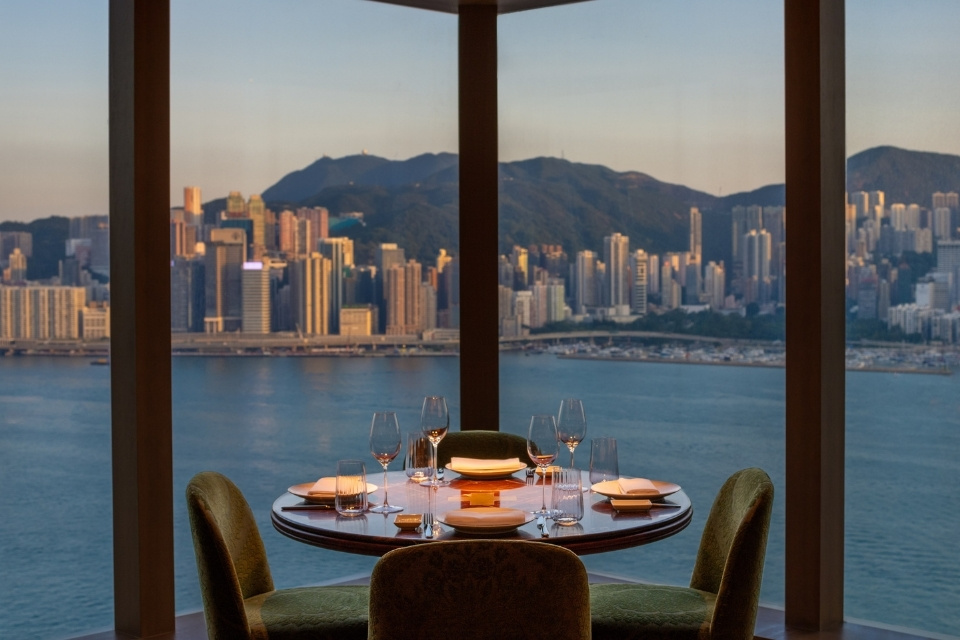 Round dining table with green chairs overlooking an ocean and cityscape