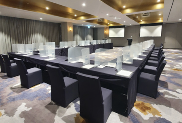 Large dark rectangular tables set up in a horseshoe with screens and patterned carpet