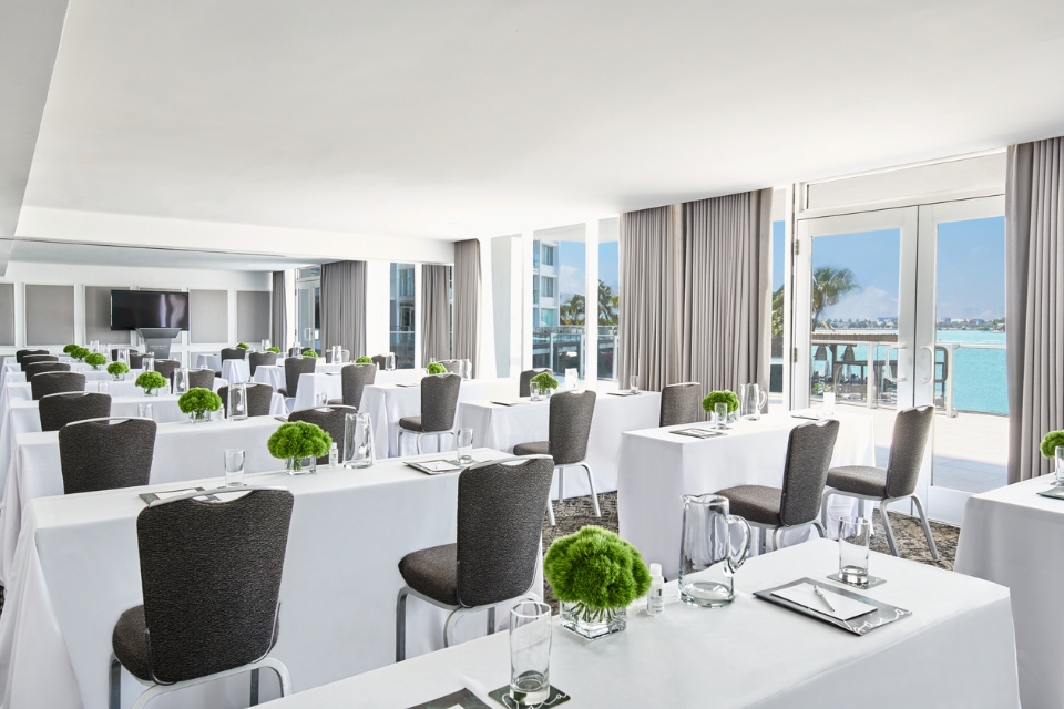 Rows of rectangular white tables with dark chairs and flowers on it