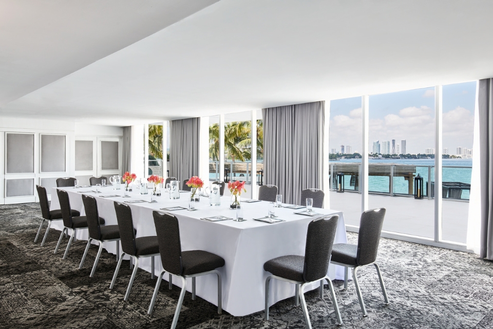 Rows of rectangular white tables with dark chairs and flowers on it