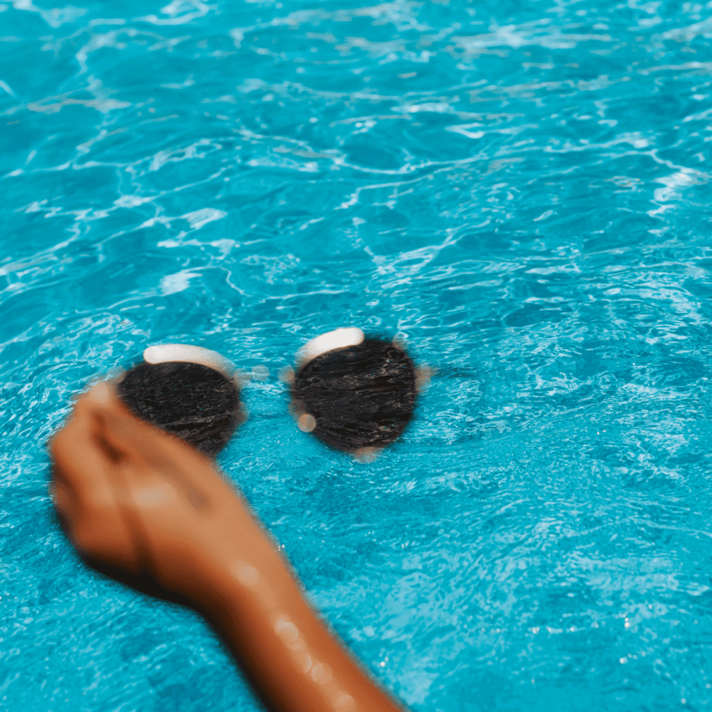hand holding a pair of sunglasses by the pool