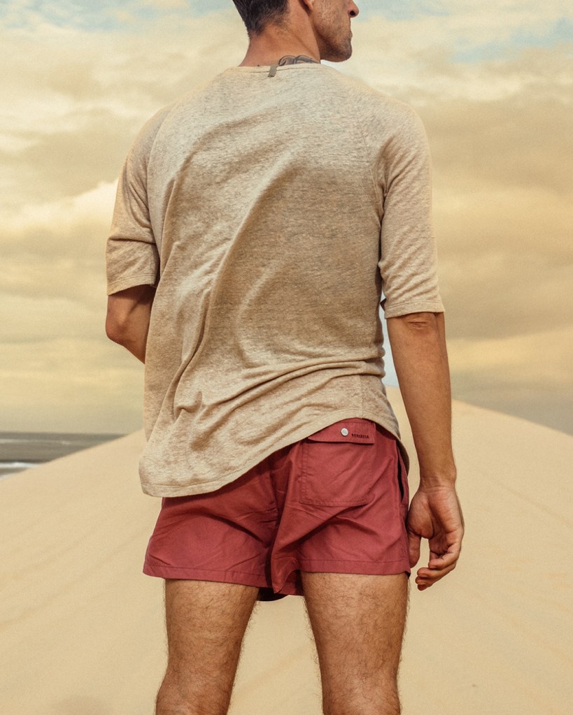 Man standing on a beach with red shorts and cream top on