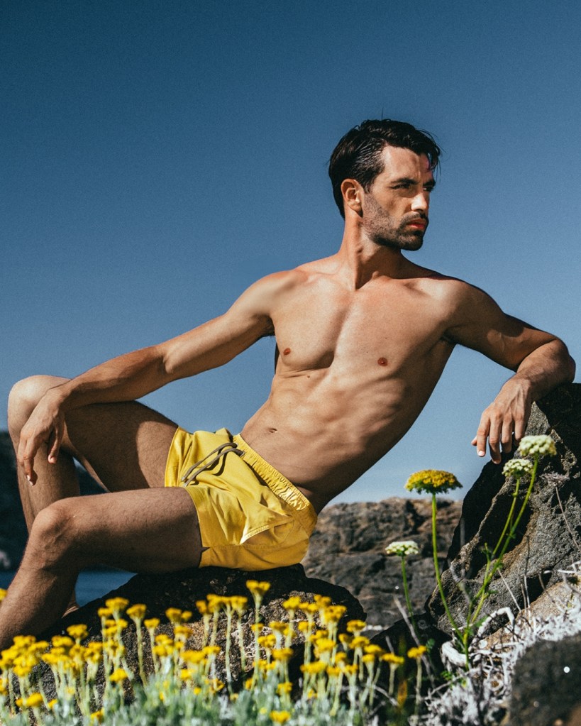 Man in yellow swim trunks sits on flowered grass