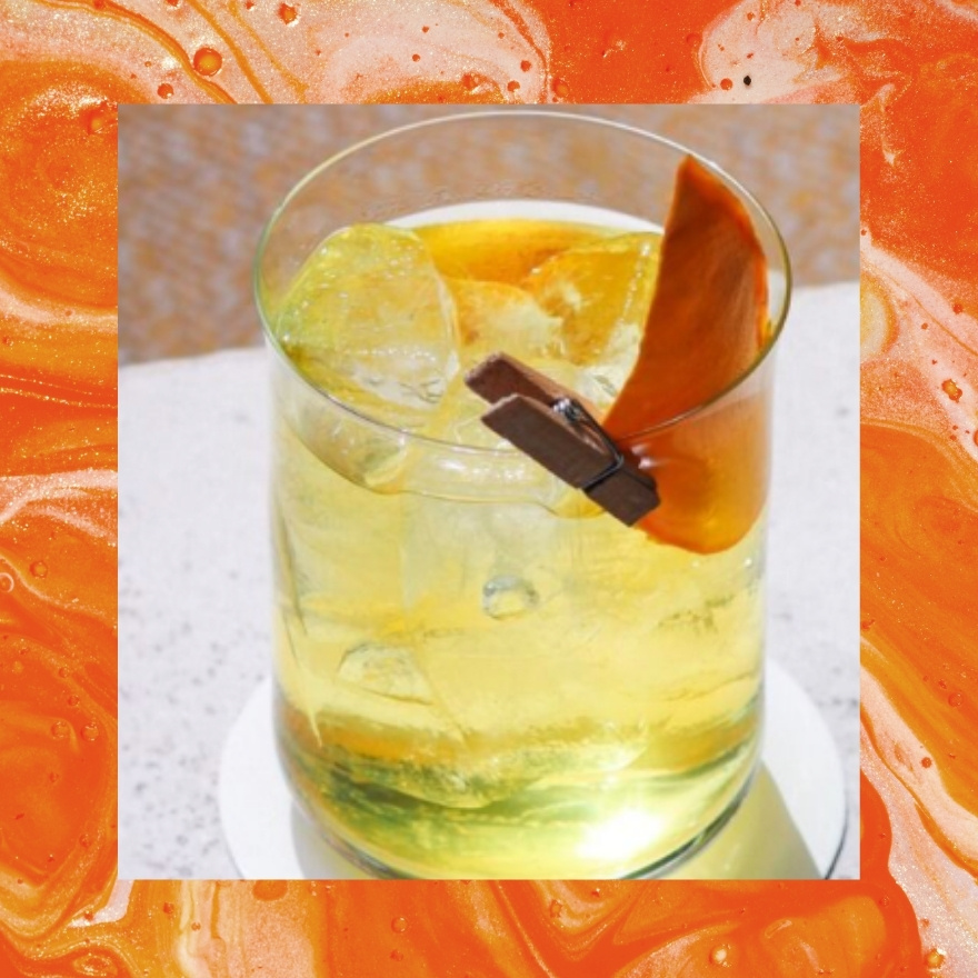 Yellow cocktail with orange slice on top of an orange border