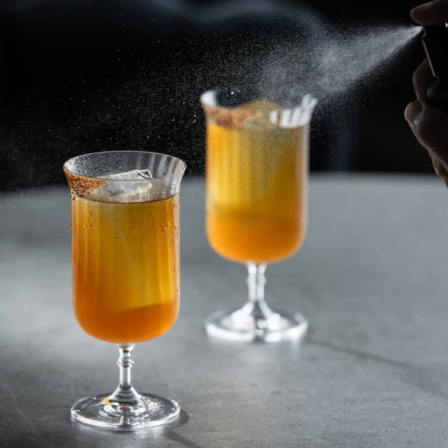 Two orange cocktails with a hand spraying them with essence