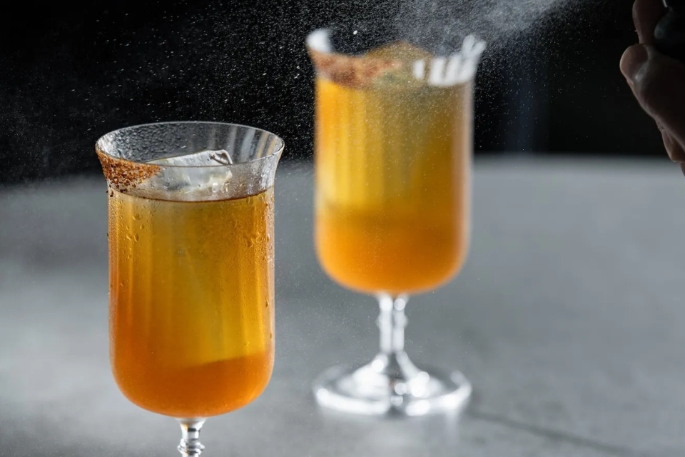 Two orange colored cocktails on a grey surface