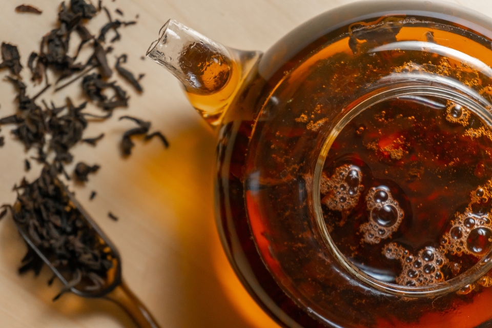 Pot of amber tea and tea leaves scattered below it