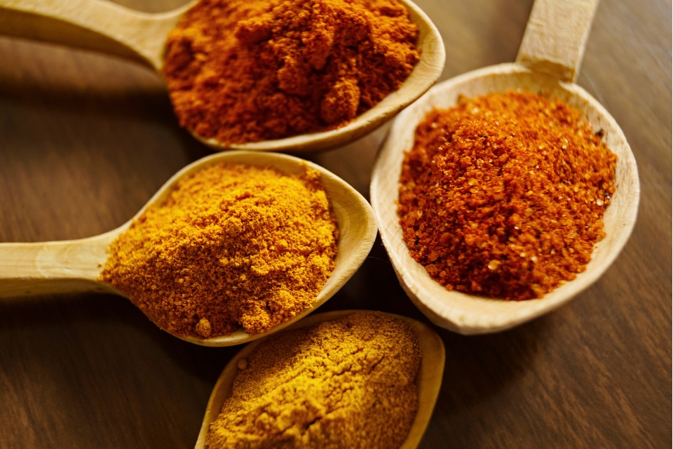 Scoops of red and yellow spices on wooden spoons