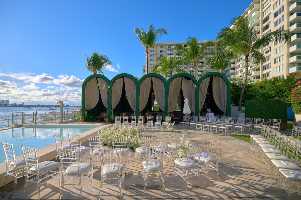 Large outdoor space set for a wedding ceremony with a pool and cabanas in the background