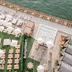Aerial view of large patio with cabanas, striped lounges, pool, and more