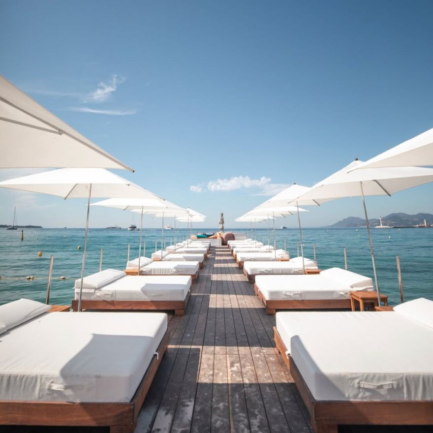 海邊甲板上擺放著兩排配有陽傘的白色長椅