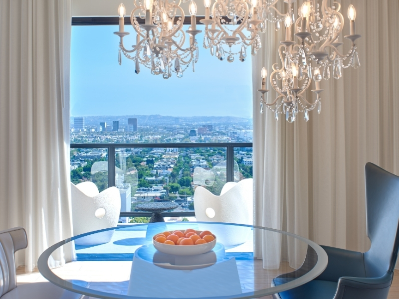Clear glass table with bowl of oranges and chandeliers overhead