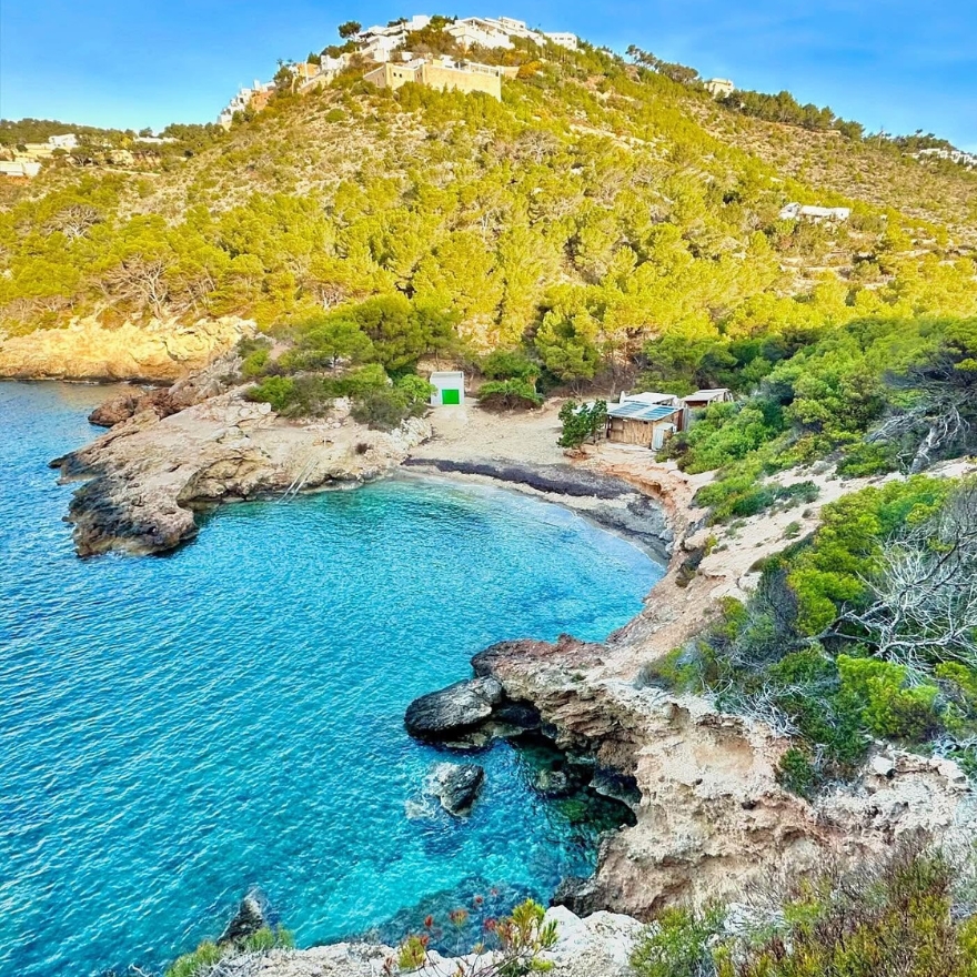 Playa con aguas azules y montañas verdes cubiertas de árboles.