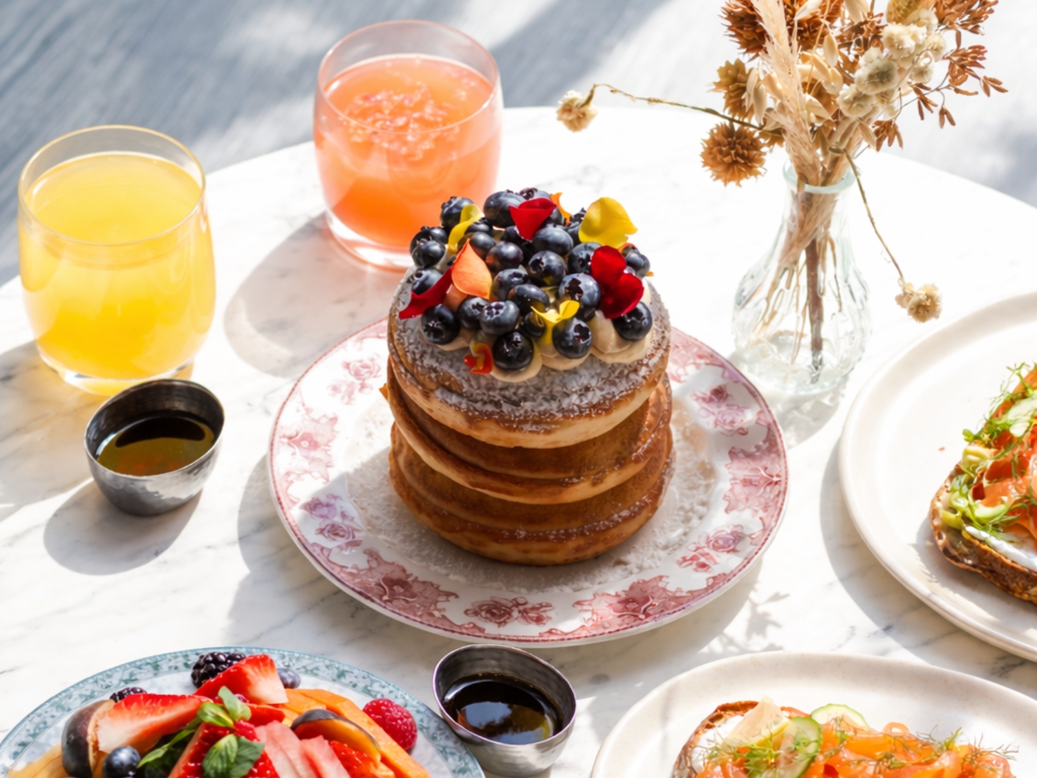 A bright and elegant breakfast spread at Mondrian Mexico City Condesa featuring fluffy berry pancakes, fresh tropical fruit, smoked salmon toast, colorful juices, and natural sunlight on a marble table in a luxury lifestyle hotel setting.