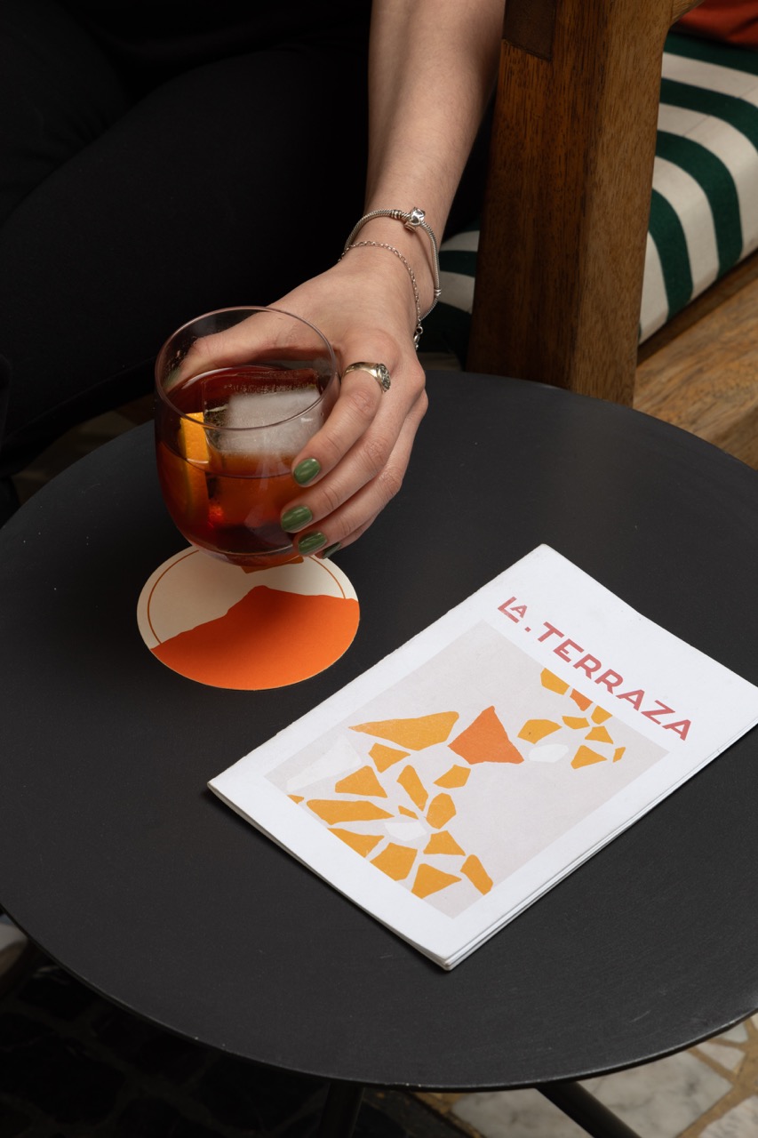 A hand holding a cup of coffee beside a Mondrian Mexico City Condesa breakfast menu on a dark table.